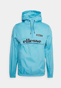 Chaqueta cortavientos azul claro con capucha, puños elásticos y un bolsillo frontal. Presenta un logo negro de "ellesse" en el pecho. Textura suave.