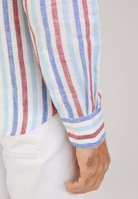 Chemise à manches courtes, à boutons, avec un motif rayé bleu, rouge et blanc. Fabriquée en tissu léger, avec un poignet et un détail de bouton.