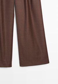 Brązowe spodnie o szerokich nogawkach z teksturowanej tkaniny o gładkim wykończeniu. Posiadają wysoki stan i swobodny krój. Wykończone starannie. 