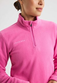 Pullover in pile rosa con colletto alto, zip frontale a metà e dettaglio del logo. Tessuto morbido, design aderente e maniche lunghe.