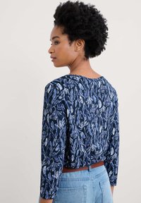 Granatowa bluzka w kwiatowy wzór z białymi i jasnoniebieskimi akcentami. Okrągły dekolt i rękawy ¾. Noszona z wysoko wartymi dżinsami.