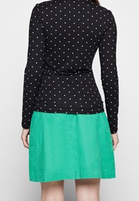 Svart långärmad topp med vita prickar, tillsammans med en texturerad grön kordskjorta. Outfiten har en figurnära silhuett och ett lagerdesign.