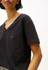T-shirt a V grigio scuro realizzato in tessuto morbido, con maniche corte e un piccolo logo sul lato sinistro del petto.