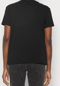 Camiseta de algodón negra de manga corta, con cuello redondo, diseño sencillo y parte trasera sin adornos. Combinada con jeans de mezclilla oscura.