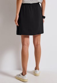 Falda negra hasta la rodilla con cintura elástica, textura suave y un diseño sencillo. Las zapatillas blancas complementan el conjunto.
