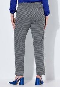 Kalhoty s černobílým kostkovaným vzorem houndstooth a slim fit. Mají zadní kapsu a jsou doplněny modrými podpatky.