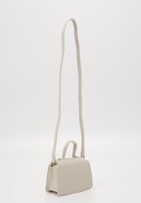 Biała torebka z sztucznej skóry krokodyla o strukturalnym kształcie, z odpinanym długim paskiem i krótkim uchwytem, cechująca się teksturowaną powierzchnią.