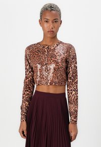 Kuttet langermet topp i brun med leopardmønster og paljett detaljer. Kombinert med en plisserte burgunder skjørt. Knapplukking foran.