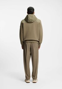 Mellembrun hoodie med hætte og teksturerede skuldre, parret med løse lysebrune bukser. Begge dele er lavet af blødt, behageligt stof.