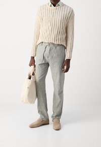 Un pull en tricot beige clair, un pantalon en lin gris, des mocassins beiges et un sac fourre-tout crème ; présente une coupe décontractée et une taille à cordon.