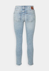 Vaqueros skinny de mezclilla azul claro con cinturilla alta, diseño de cinco bolsillos y una etiqueta de cuero marrón en la parte trasera de la cintura. Estilo clásico con una textura suave.