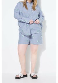 Chemise rayée bleu et blanc avec broderie florale, assortie à un short rayé assorti. Le mannequin porte des sandales noires et blanches.