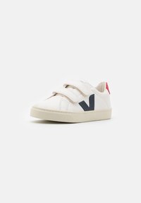 Witte sneaker met twee klittenbandsluitingen, marineblauw logo detail, rode accenten op de hiel en een gestructureerde rubberen zool. Gladde leren materia.