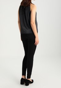 Černý bezrukávový top s texturovaným povrchem, se skládacím výstřihem a detaily na zavazování na zadní straně, ve spojení s úzkými černými kalhotami a botami na blokovém podpatku.