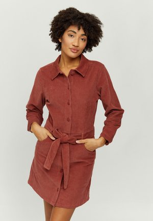 Corduroy dress in rust color, featuring a button-up front, long sleeves, collar, and a waist belt with pockets for added detail.