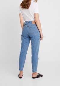 Ljust blå högmidjade jeans med rak passform, fransad nederkant och märkets läderpatch på den bakre midjebandet. Svarta platta sandaler.