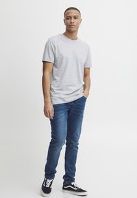 Tricou gri cu mânecă scurtă, prevăzut cu un buzunar pe piept, asortat cu blugi slim-fit albaștri și adidași negri cu șireturi și talpă albă.