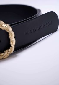 Ceinture en cuir noir avec une boucle en métal doré twisted. Présente le texte embossé "MISEAUGREEN" sur la sangle. Texture lisse et design élégant.