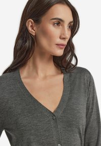 Grauer Cardigan mit V-Ausschnitt, weichem Material und Knopfverschluss. Der Stoff wirkt leicht und glatt.