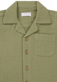 Zielona koszula z fakturowanej tkaniny, z kołnierzykiem, drewnianymi guzikami, pojedynczą kieszenią na piersi oraz marszczonym wzorem materiału.