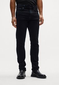 Jeans oscuros de mezclilla, con un diseño ajustado, cinco bolsillos y cierre de cremallera. Combinados con botas de cuero negras.