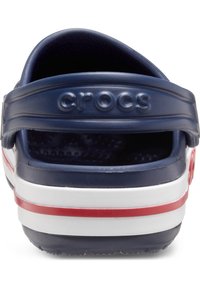 Crocs blu navy e bianchi con strisce rosse, dotati di cinturino posteriore e interno testurizzato. Il materiale morbido evidenzia durata e comfort.