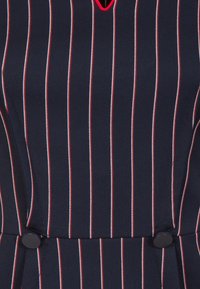 Marine jurk met verticale witte en rode strepen. Bevat een V-halslijn en zwarte knopen bij de taille. Textuurstof met een getailleerde pasvorm.