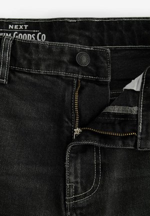 Zwarte denim jeans met een gouden rits, zichtbare stikseldetails en een metalen knoop. De binnenkant heeft een witte stofvoering nabij de rits.