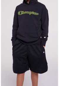 Černá mikina s kapucí s neonově zeleným logem "Champion" a přední kapsou. Černé síťované šortky s bočními kapsami a logem Champion na lemu.