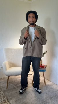 Blazer a righe marroni con grandi bottoni sopra una t-shirt bianca, abbinato a jeans scuri e sneakers bianche e nere. Sfondo neutro.