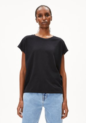 T-shirt en coton noir avec une coupe décontractée et des manches courtes roulées, associé à un jean en denim bleu clair. Design simple et couleur unie.