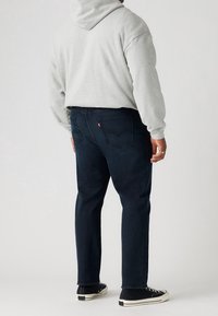 Huppari harmaalla värillä, jossa on huppu, yhdistettynä tummansinisiin farkkuihin, joissa on takataskut. Mustat kengät valkoisilla pohjilla täydentävät asua.