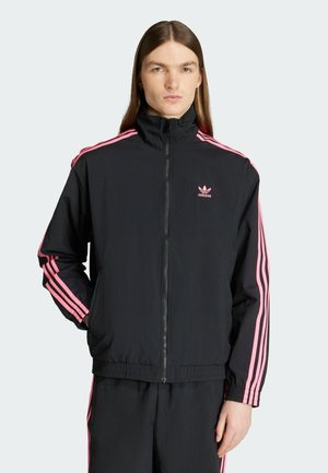 Zwarte zip-up trainingsjack met roze drie-strepen accenten op de mouwen. Gemaakt van lichtgewicht materiaal met een opstaande kraag.
