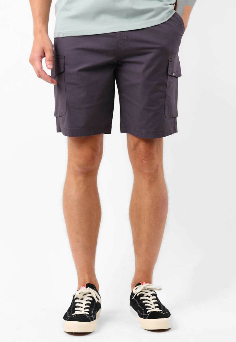 Shorts de cargo bleu marine avec deux poches latérales, une texture lisse et une coupe droite. Portés avec des baskets noires dotées de lacets et de semelles blanches.