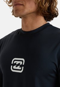 Mörk marinblå kortärmad träningsskjorta med en framträdande vit logotyp på bröstet, tillverkad av stretchigt, fuktavvisande material.