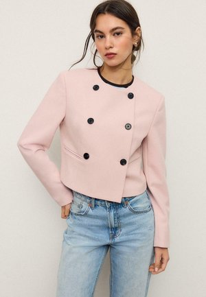 Kvinde iført en lyserød dobbeltknappet cropped blazer med sorte knapper og lyseblå højttaljede jeans.