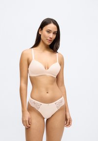 Jasnoróżowy biustonosz z głębokim dekoltem i regulowanymi ramiączkami, w zestawie z dopasowanymi majtkami z koronkowymi akcentami po bokach i gładkim materiałem.