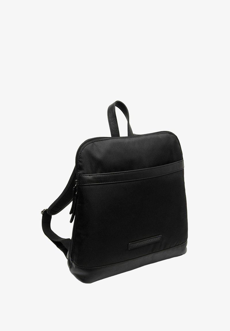 Mochila negra de nylon con base de cuero, forma rectangular, doble tira para el hombro, asa superior y un bolsillo frontal con cremallera. Textura suave, diseño minimalista.