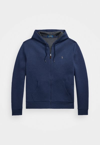 Granatowy hoodie na zamek wykonany z mieszanki bawełny. Ma sznurek przy kapturze, kieszenie z przodu oraz małe logo na piersi.
