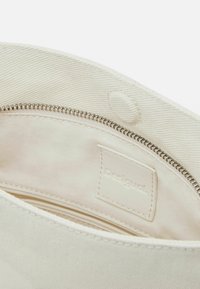 Interno della borsa in tela di un beige chiaro con una texture liscia, caratterizzato da una cerniera argentata e da un'etichetta con logo. Design a tasca singola.