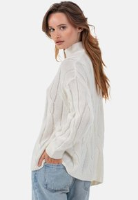 Weißer Pullover mit Zopfmuster und hohem Kragen, mit lockerem Schnitt und gerippten Bündchen. Weiche Textur und entspannte Silhouette.