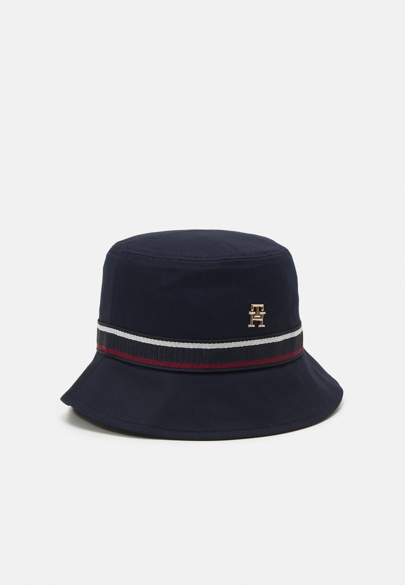 Chapeau bob bleu marine à large bord, avec un bandeau rayé noir, blanc et rouge, et un petit emblème doré sur le côté.
