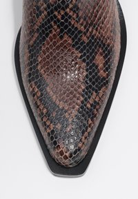 Botín tobillo de punta fina hecho de cuero con estampado de serpiente en tonos marrón y negro, que cuenta con una suela negra elegante y un patrón geométrico.
