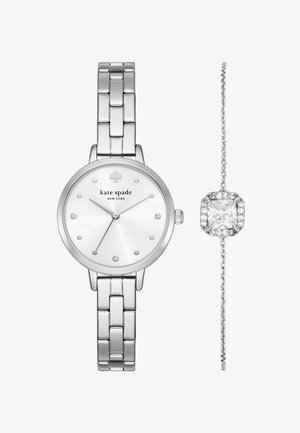 Zilveren horloge met een ronde wijzerplaat, witte wijzerplaat, diamanten accenten en een RVS band. Vergezeld door een delicate zilveren armband met een heldere edelsteen.
