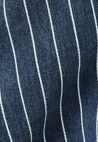 Tejido de mezclilla con rayas blancas verticales sobre un fondo azul oscuro, con un acabado texturizado que realza la profundidad y el interés visual.