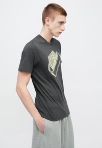 Tmavosivá bavlnená tričko s okrúhlym výstrihom a veľkým svetlosivým logom Nike na prednej strane. K dispozícii vo vypracovanom strihu.