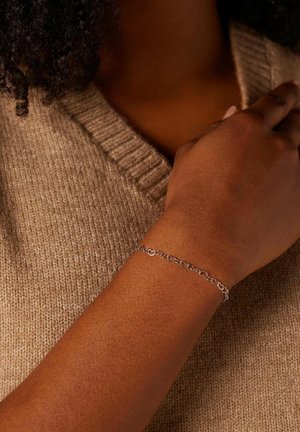 Zilveren armband met geschakelde cirkels, geplaatst op een donkere huidtoonpols, tegen een gestructureerde beige trui.