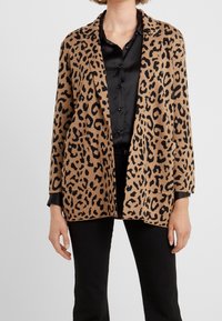 Kašmírový cardigan s leopardím vzorem v hnědé a černé barvě, vyrobený z měkké tkaniny, otevřený design, dvě našité kapsy, s dlouhými rukávy.