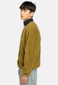Olivengroen fleece sweatshirt met een zwarte kraag; heeft een ontspannen pasvorm, lange mouwen en een zachte, textuurrijke oppervlakte.