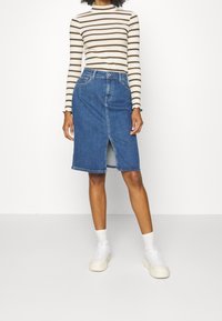 Jeanskjol med medellång klippning, framtida slits och klassisk blå färg. Kombinerad med en randig långärmad topp och vita sneakers.